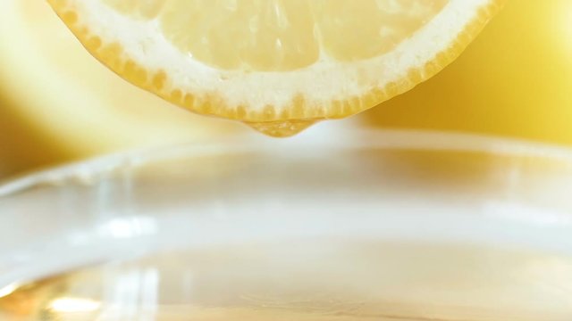 Closeup slow motion video of droplet of juice falling from lemon slice in gla