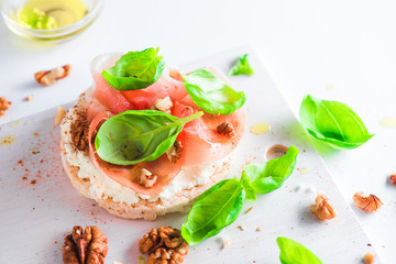 Crisp bread healthy snack with Parma ham, soft cottage cheese, walnuts, olive oil, paprika, fresh basil leaves. Easy breakfast close-up on a white background with copy space.
