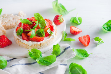 Healthy snack with crisp bread, fresh strawberries, goat cheese, and basil leaves. Easy breakfast close-up on a white background with copy space.