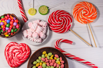 Colorful chocolate candies, lollipops, candy cane and marshmallows on wooden table