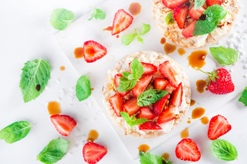 Healthy snack with crisp bread, fresh strawberries, soft creme cheese, mint, balsamic vinegar. Easy breakfast close-up on a white background with copy space.