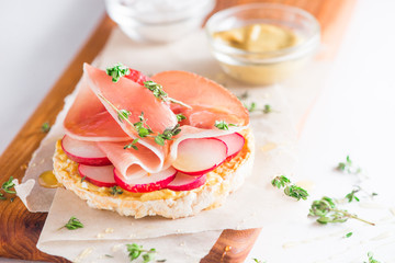 Crisp bread healthy snack with Parma ham, radish slices, mustard, sea salt, honey and fresh thyme. Easy breakfast close-up on a white background with copy space.