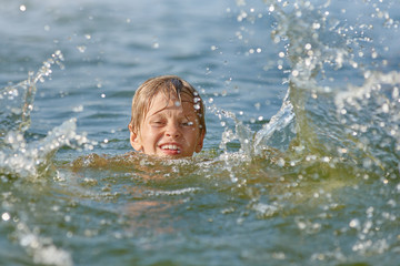 Portrait of young serious boy swimming in the lake at summer