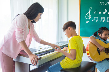 Young asian boy playing music keyboard with his teacher in classroom