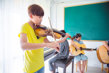 Young asian boy playing violin in classroom with his friends
