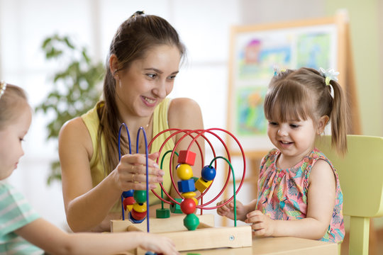 Young kindergarten teacher helping kids girls with toys