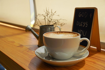 A cup of coffee in the moring with blessing message "God bless you" on a blackboard in warm lighting tone