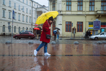 reflection on young woman in red coat in puddle. rainy weather. yellow umbrella