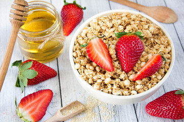 Delicious granola with fresh strawberries in a white plate with honey and sesame, healthy breakfast, healthy diet, view from above