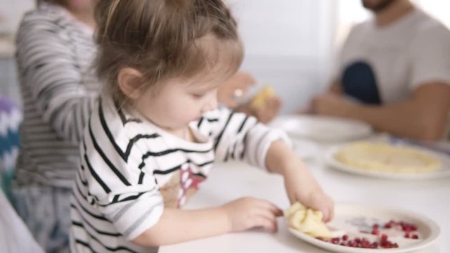 Funny little girl is licking the condensed milk from the pancake while mother feeds the cat. Family breakfast