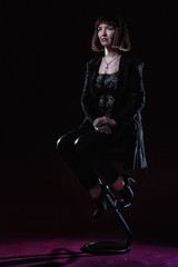 Obraz na płótnie Canvas Confident ugly woman wearing black suit siting and posing in front of camera on stage with crimson floor
