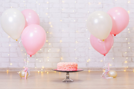 birthday celebration background - pink cake over brick wall with lights and balloons