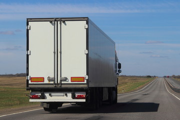 Transportation logistics - white semi trailer truck on asphalt road in summer on blue sky background, rear view