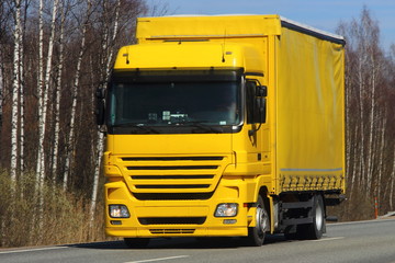 Fototapeta na wymiar Transportation logistics - yellow truck with yellow semi-trailer on asphalt road in spring against blue sky forest, front view