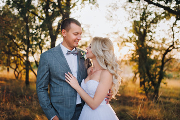 Beautiful and stylish newlyweds are hugging amidst the chic nature at sunset. The groom smiles and hugs the bride with curly hair. Portrait of a newlywed couple.