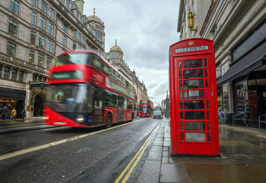 London, England - Iconic blurred red double-decker buses on the move with traditional red telephone box in the center of London at daytime