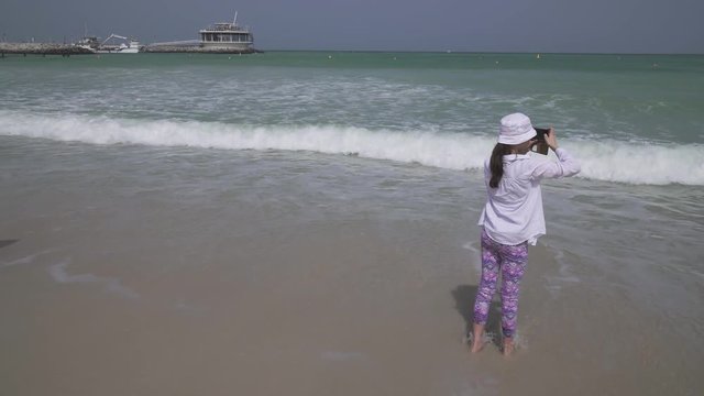 Teenage girl takes pictures of the sea waves of the Persian Gulf on smartphone on the beach of Dubai stock footage video