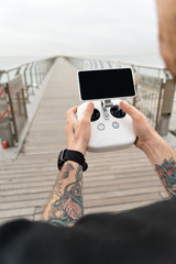 Young professional or amateur photographer or drone pilot holds remote control panel with screen and controls ready to fly quadrocopter in air to see birds point of view.Hipster user of new technology