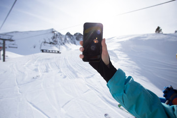 Skier or snowboarder woman holds up smartphone with big screen up in air, looks for network...