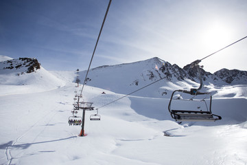 Fototapeta na wymiar View of ski and snowboard slopes landscape up in mountains winter sports resort, ski lift machine transports skiers and snowboarders to top of mountain on clear sunny day, perfect for winter vacation