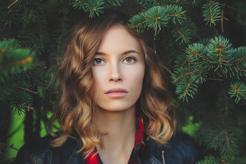 Beautiful face of a young woman against a background of fir branches. Outdoor portrait in autumn park