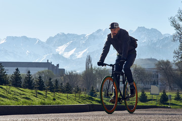 Fototapeta premium A man with the black bicycle goes against the background of big mountains in the city of Almaty