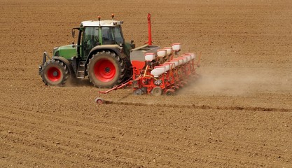Tractor with a modern sowing seeds machine in a newly plowed field in springtime. Side back view,...