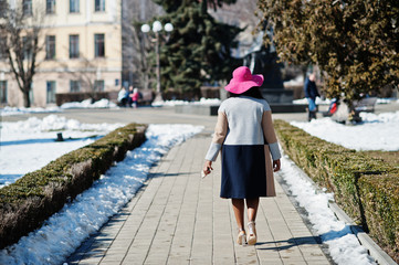 African american woman at hat and coat with phone walking at streets.