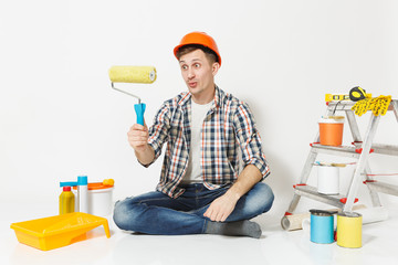 Man in orange protective helmet sitting on floor using paint roller. Instruments for renovation apartment isolated on white background. Wallpaper, gluing accessories, painting tools. Repair concept.