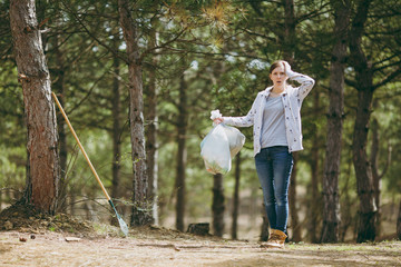 Fototapeta premium Young shocked woman cleaning rubbish holding trash bags and clinging to head in park on green background. Problem of environmental pollution. Stop nature garbage, environment protection concept.