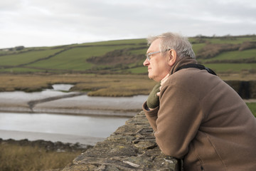 Worried looking mature man contemplating outdoors with fields in the background 