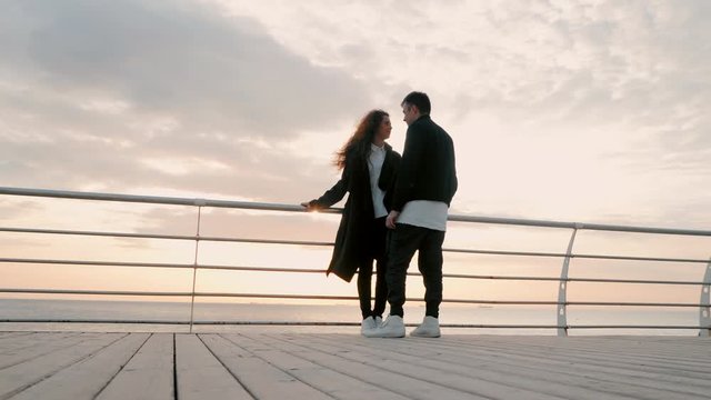 Young happy couple in love. Pair standing on wooden pier near sea or ocean and smiling to each other. People in black and white trendy clothing, They enjoying life. Romantic concept. 4k