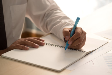 Success businessman hand holding pink marker pen on hand and writing idea or somethings on notebook with business paper on wooden table in office.