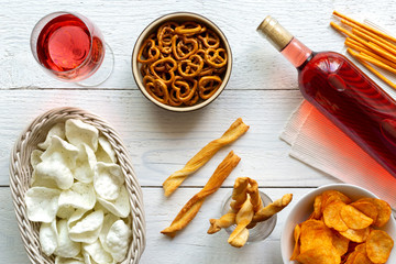 Rose wine with savoury party snacks on rustic white wood background from above.