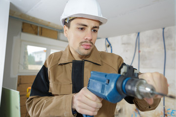 young man using power drill on wall at home