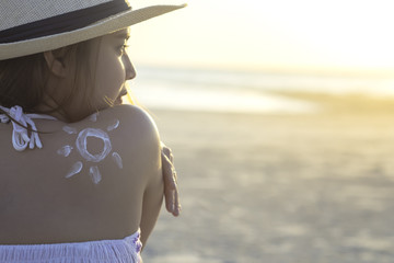 Attractive young woman traveler using skincare sunblock cream for sun protection on summer tropical beach lifestyle. Sunscreen lotion in sun shape on tan skin shoulder protect sunburn and skin cancer.