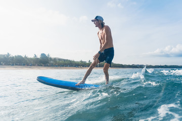 side view of man in swimming shorts and cap surfing in ocean