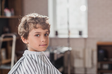 adorable little kid covered with striped cloth at barbershop