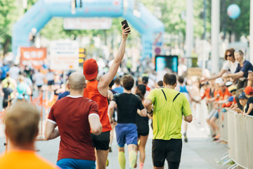 Mann macht freudig ein Foto beim Laufen mit Smartphone beim Marathon