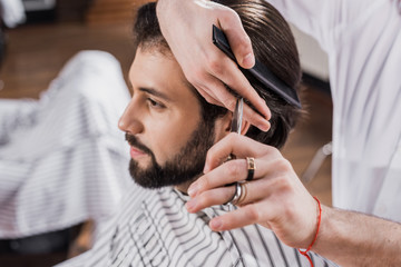 cropped shot of barber cutting hair of customer with scissors