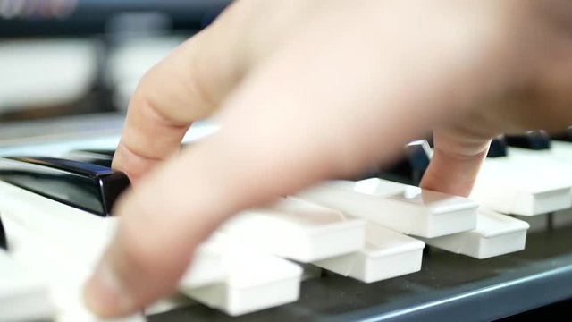 White and black synthesizer keys. The pianist's hand plays on the electronic piano at the recording studio