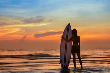 Fototapeta na wymiar woman holding a surfboard in hand laying on back beside, on returning home station after played surf in the sea at sunset