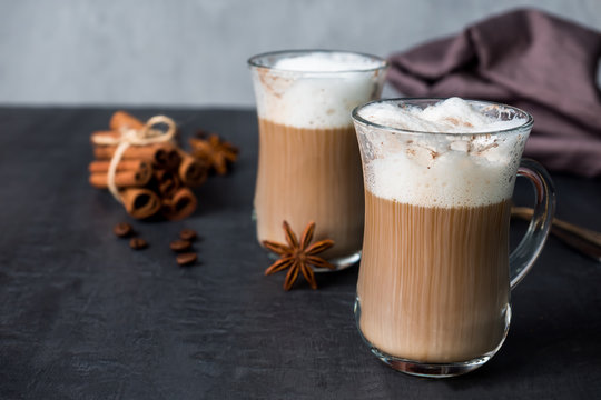 Coffee with rich milk foam in a glass beaker on a dark background sticks of cinnamon and stars of anise. Copy space