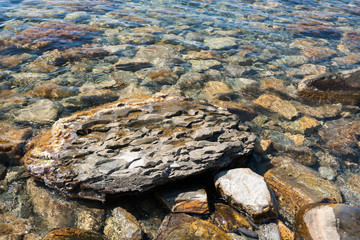 Close-up a large flat textured stone in transparent sea water.