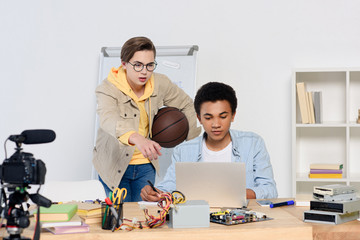 caucasian teenager pointing on something at laptop to african american friend at home