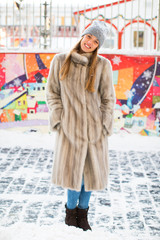 Portrait of a young woman in a blue knitted hat and gray mink coat