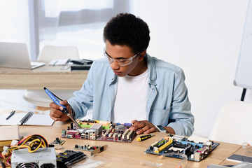 african american teenager soldering computer circuit with soldering iron at home - obrazy, fototapety, plakaty