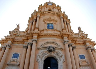 Fototapeta na wymiar Façade of the baroque Duomo di San Giorgio or Cathedral of San Giorgio in Ragusa Ibla, Sicily, Italy, containing massive ornate columns, statues of saints and decorated portals 