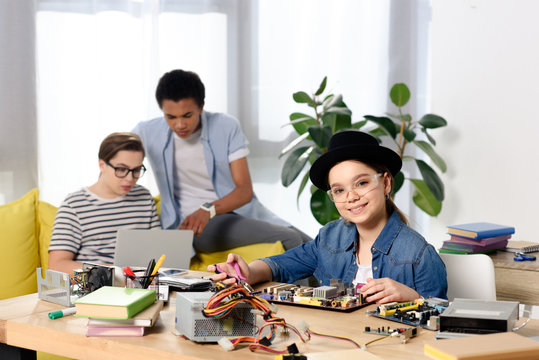 Multicultural Teen Boys Using Laptop And Female Kid Fixing Computer Motherboard At Home