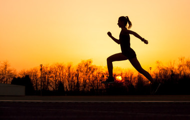 Silhouette of running woman at sunset with sun in the background
